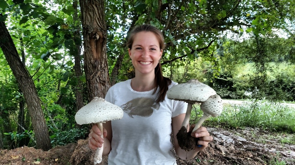 female student holding large mushrooms in the woods